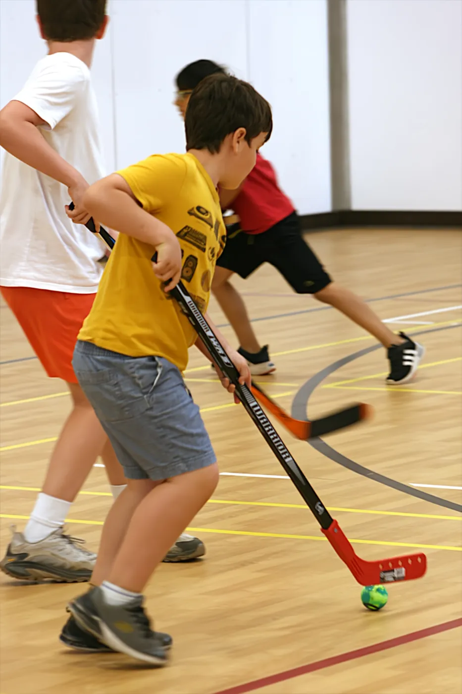 Two young ball hockey players racing for a green ball with their sticks during an indoor game at the RA Centre.