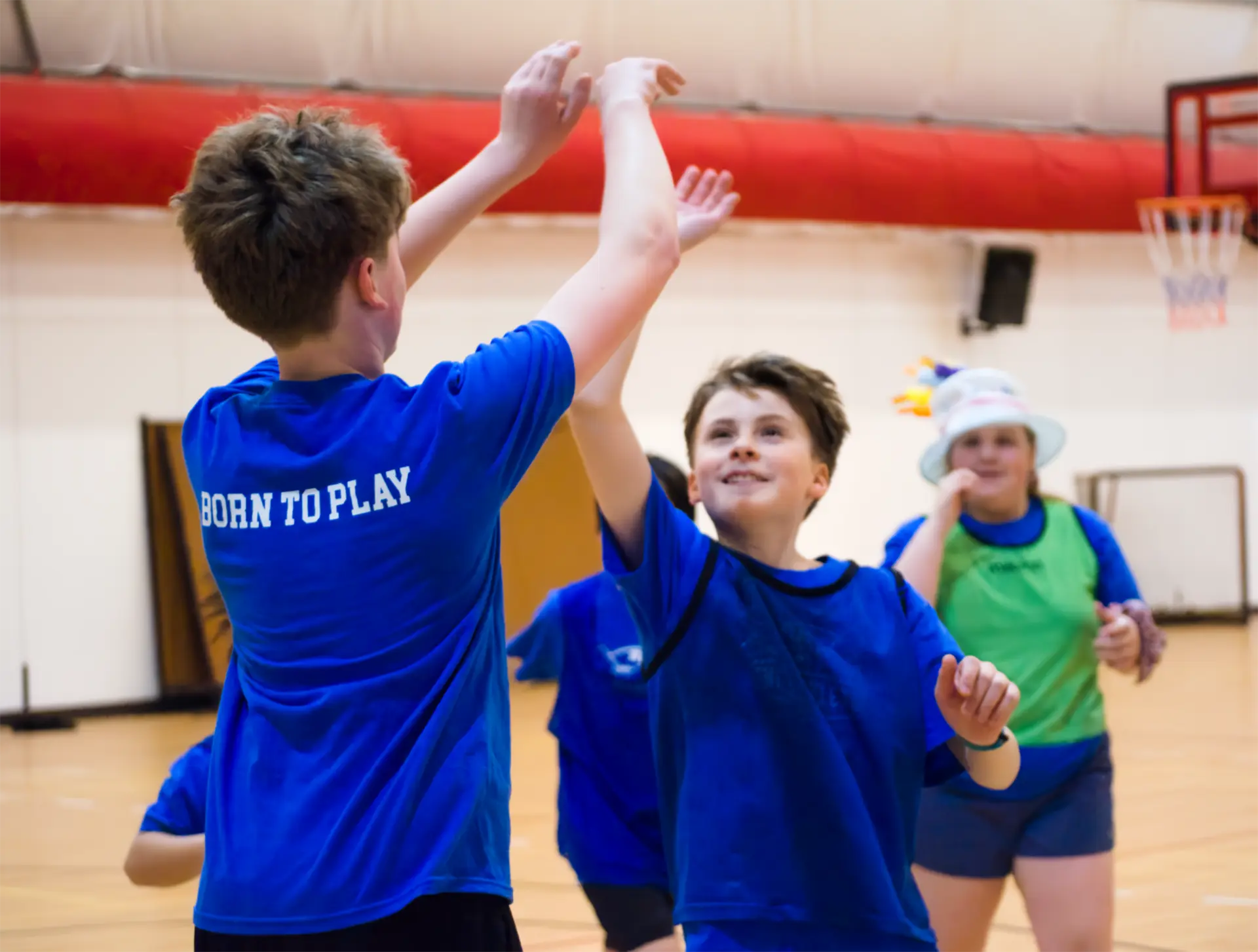 Two young basketball players in blue Junior Athletes shirts celebrating with a high-five in the gym.