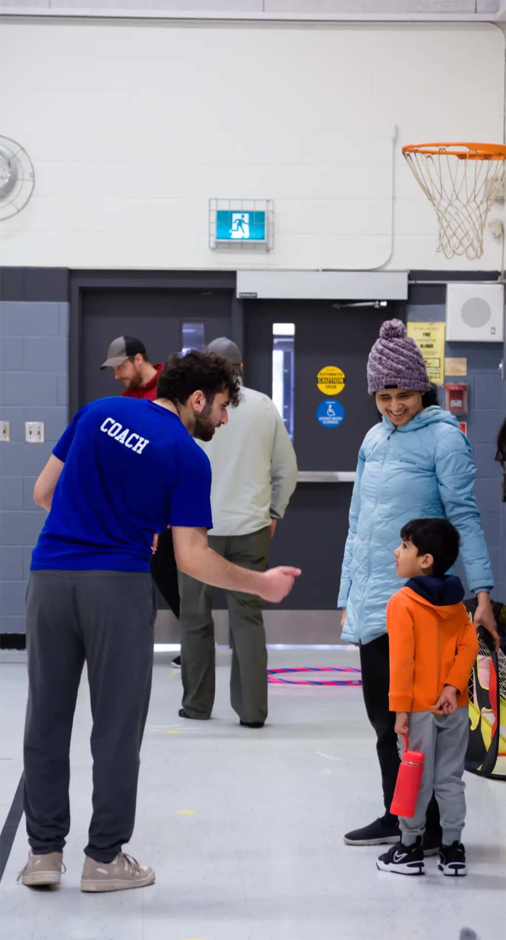 A Junior Athletes coach welcoming a young athlete and their parent into the gym before a Sunday morning session in Kanata.